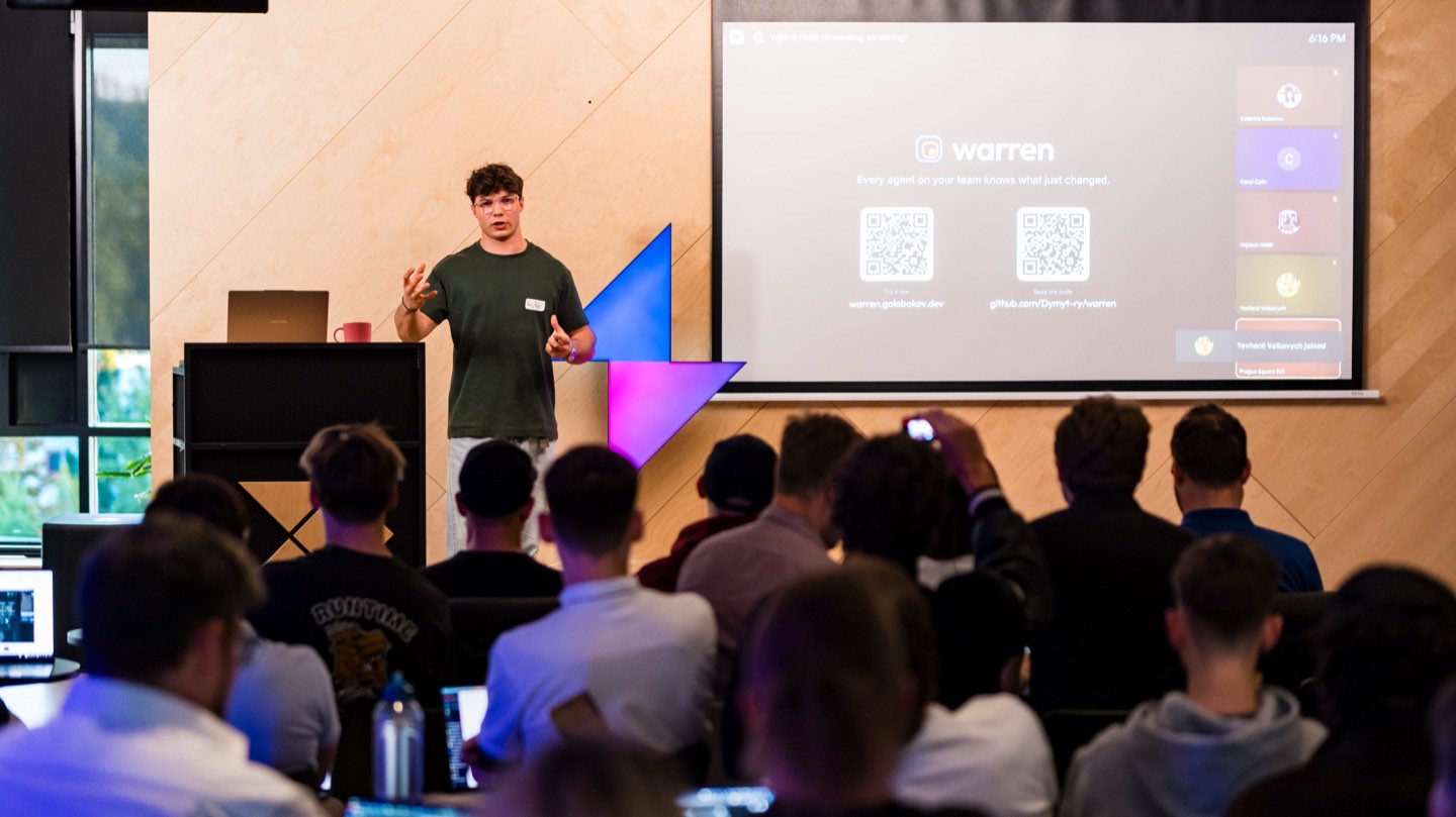 A teammate pitching warren on stage in front of a slide with QR codes for the live site and the GitHub repository
