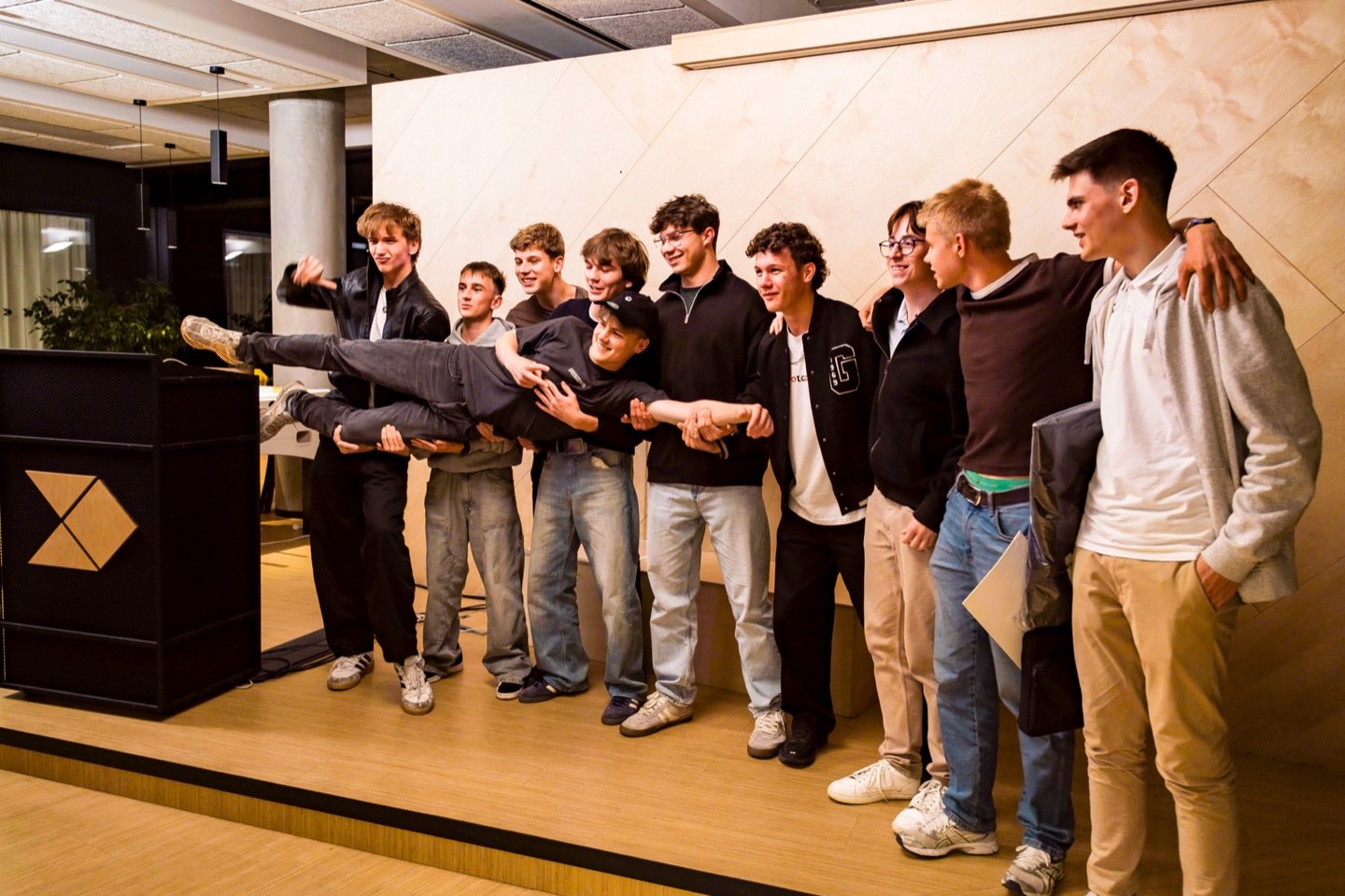 A group of participants posing on stage, one of them held horizontally across the others’ arms